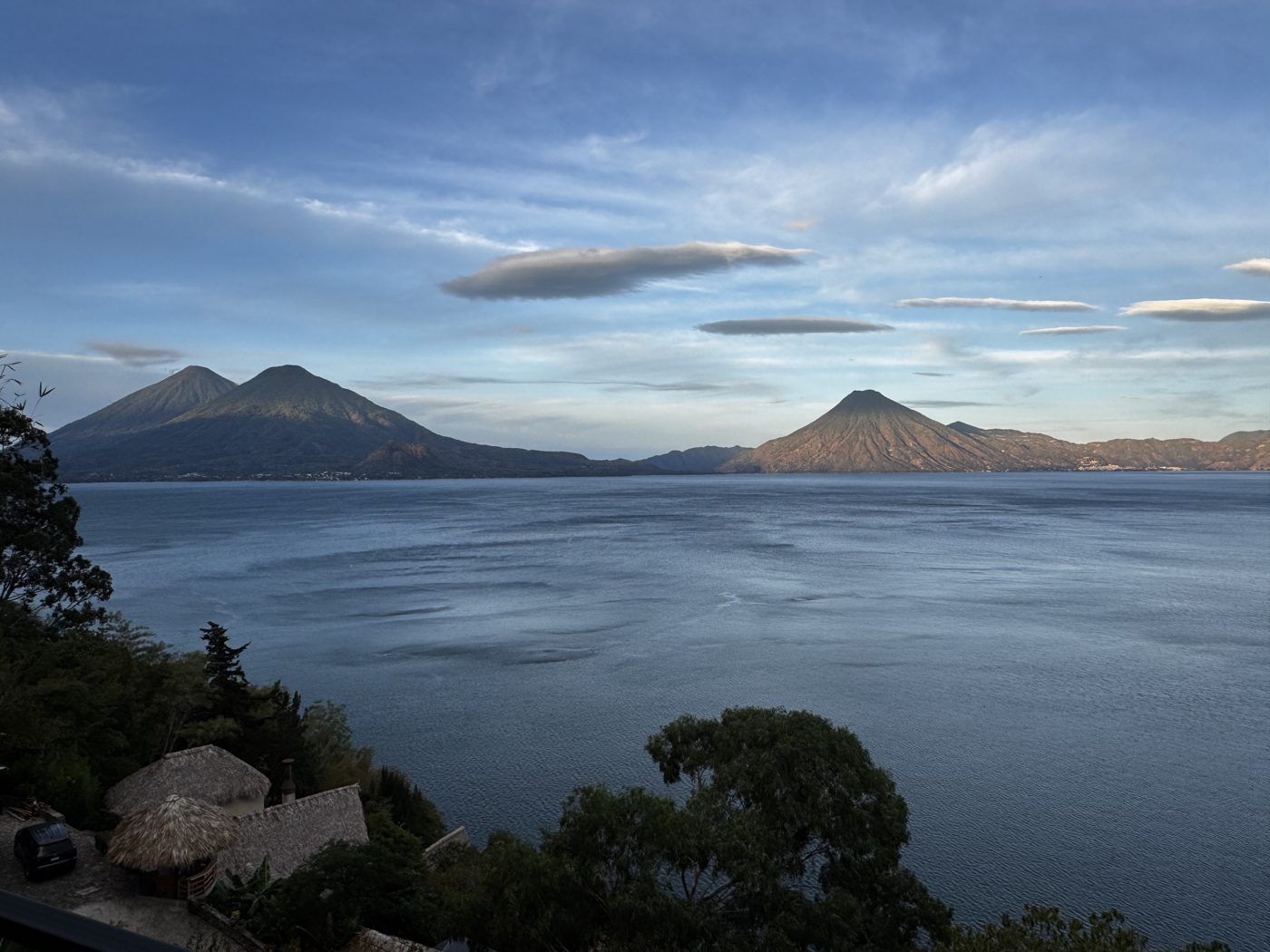 Evening view of Lake Atitlan with volcanoes and a thatched-roof terrace